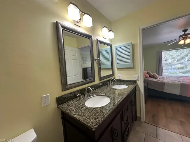 Bathroom with dual sinks, tile flooring, vanity with extensive cabinet space, and ceiling fan