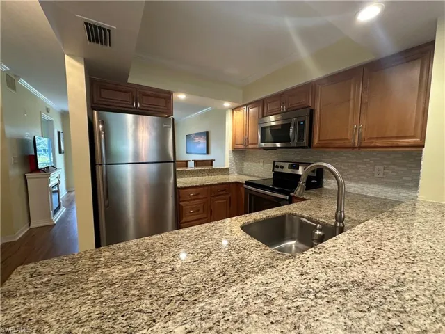 Kitchen with hardwood / wood-style floors, tasteful backsplash, light stone counters, sink, and appliances with stainless steel finishes