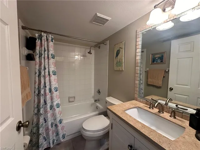 Full bathroom featuring vanity with extensive cabinet space, toilet, tile flooring, shower / bath combo with shower curtain, and a textured ceiling