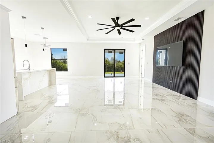 Empty room featuring a raised ceiling, ceiling fan, plenty of natural light, and ornamental molding