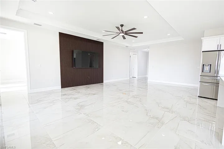 Unfurnished living room with a raised ceiling, ceiling fan, and ornamental molding