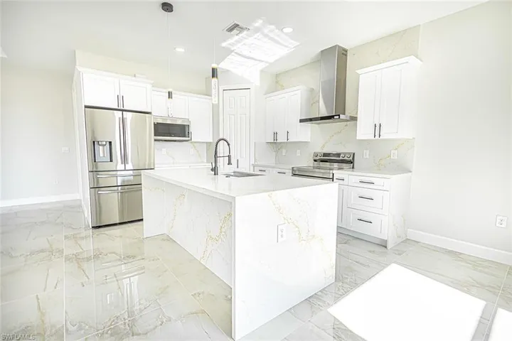 Kitchen with sink, stainless steel appliances, wall chimney range hood, a center island with sink, and white cabinets