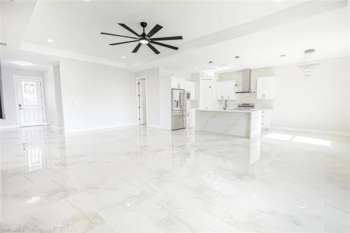 Unfurnished living room with a raised ceiling, ceiling fan, ornamental molding, and sink