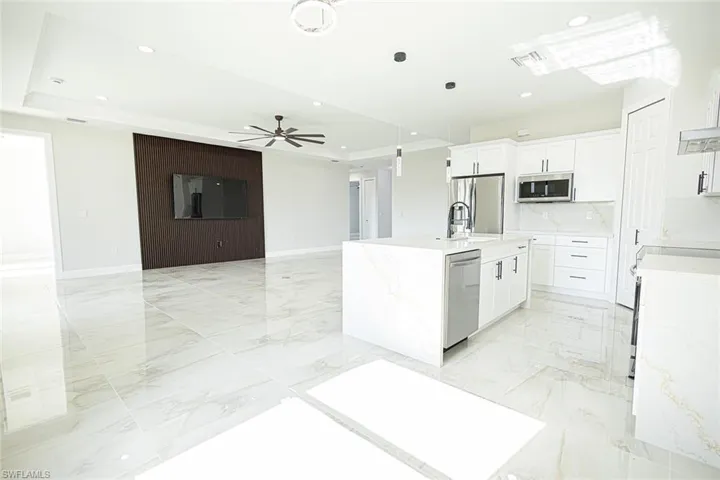 Kitchen with backsplash, ceiling fan, an island with sink, white cabinetry, and stainless steel appliances