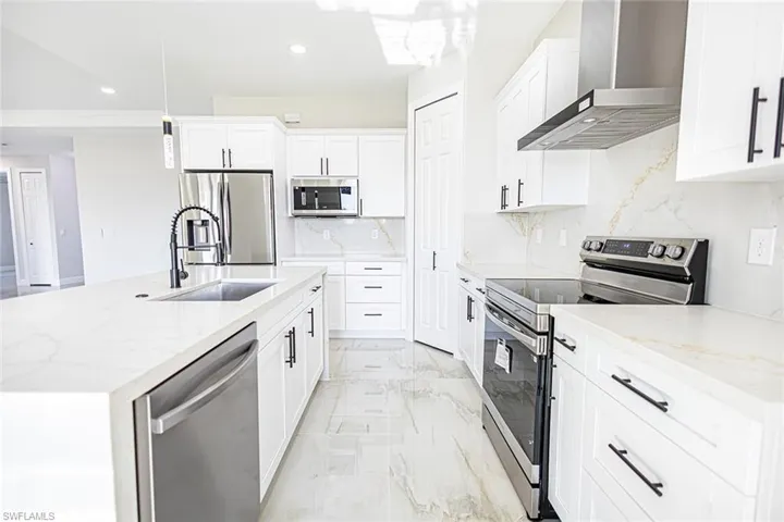 Kitchen with pendant lighting, sink, wall chimney exhaust hood, white cabinetry, and stainless steel appliances