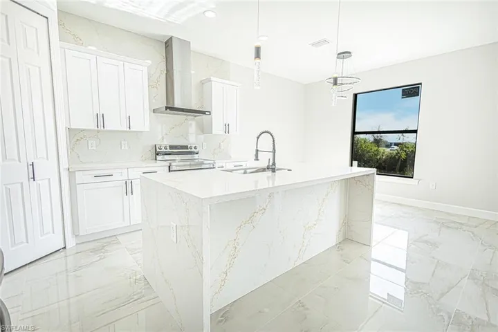 Kitchen with sink, wall chimney range hood, decorative light fixtures, a center island with sink, and white cabinetry