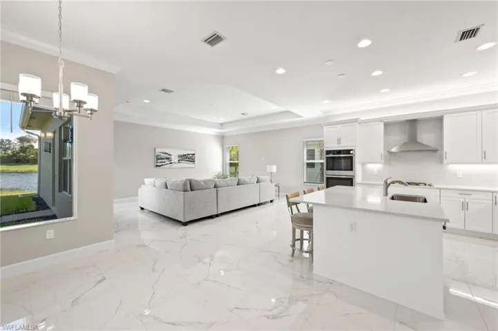 Kitchen with stainless steel double oven, wall chimney range hood, a kitchen breakfast bar, decorative light fixtures, and white cabinets