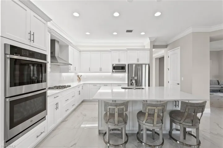Kitchen with white shaker cabinets, a center island with sink, a kitchen breakfast bar, wall chimney exhaust hood, and stainless steel appliances