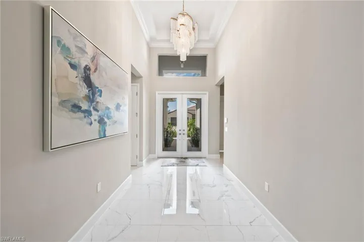 Entryway featuring french doors, a notable chandelier, crown molding, and a high ceiling