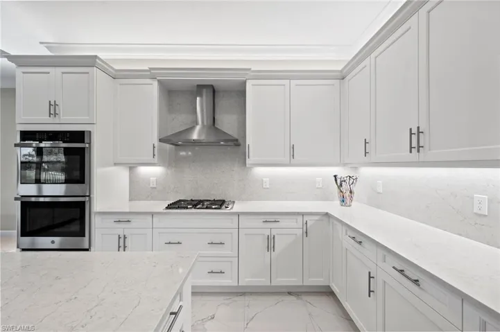 Kitchen featuring wall chimney exhaust hood, white cabinetry, light stone countertops, and stainless steel appliances