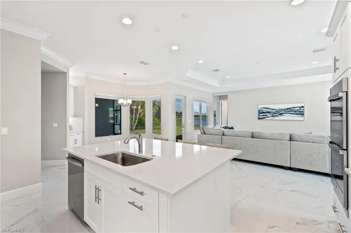 Kitchen with sink, white cabinetry, stainless steel appliances, crown molding, and a kitchen island with sink