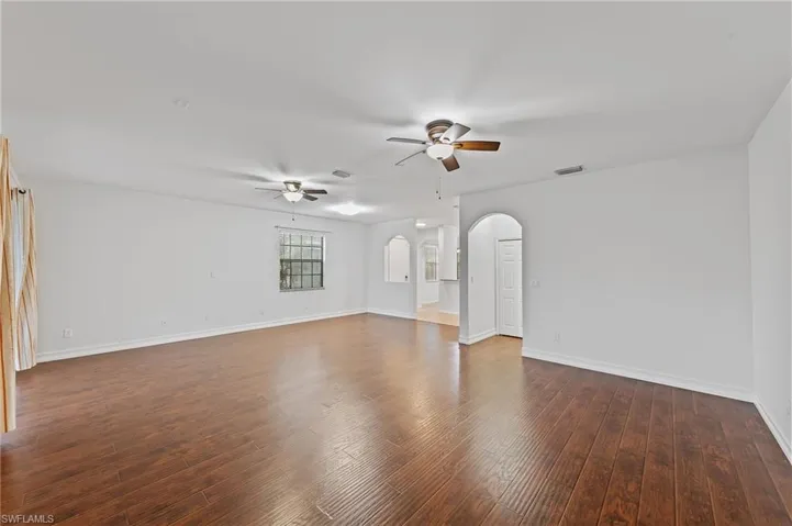 Spare room featuring arched walkways, dark wood finished floors, and a ceiling fan