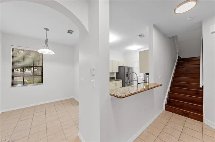 Kitchen with light tile patterned floors, light stone counters, high end fridge, a peninsula, and decorative light fixtures