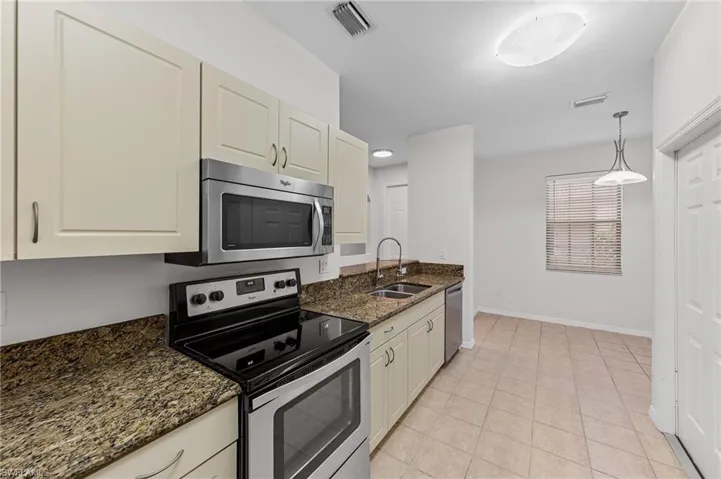 Kitchen featuring appliances with stainless steel finishes, hanging light fixtures, dark stone countertops, and light tile patterned floors