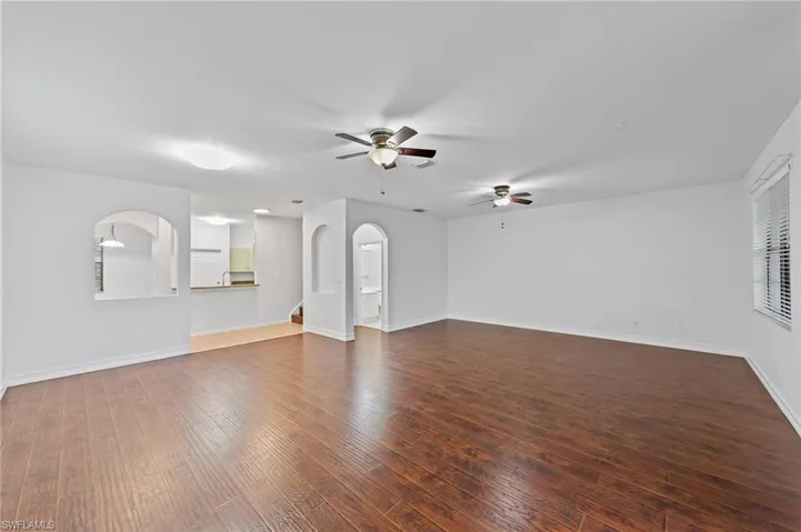 Unfurnished living room with dark wood finished floors, arched walkways, and ceiling fan