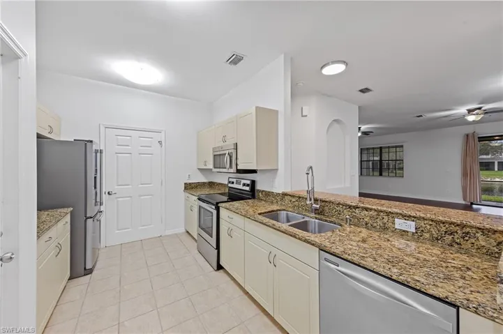 Kitchen with stainless steel appliances, light stone countertops, ceiling fan, and light tile patterned flooring