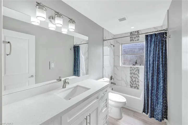 Full bath featuring vanity, shower / bath combo, and light wood-style floors