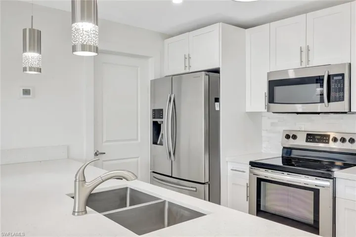 Kitchen featuring stainless steel appliances, white cabinetry, tasteful backsplash, decorative light fixtures, and light stone counters