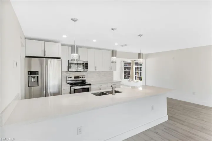 Kitchen with appliances with stainless steel finishes, hanging light fixtures, backsplash, white cabinets, and recessed lighting