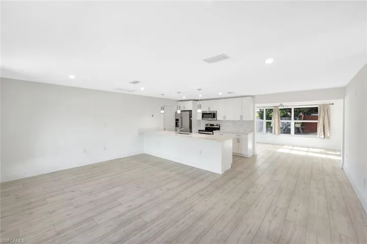 Kitchen with open floor plan, white cabinetry, decorative backsplash, a peninsula, and stainless steel appliances