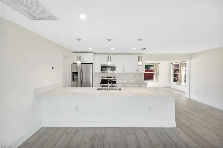 Kitchen featuring stainless steel appliances, white cabinetry, tasteful backsplash, a peninsula, and hanging light fixtures
