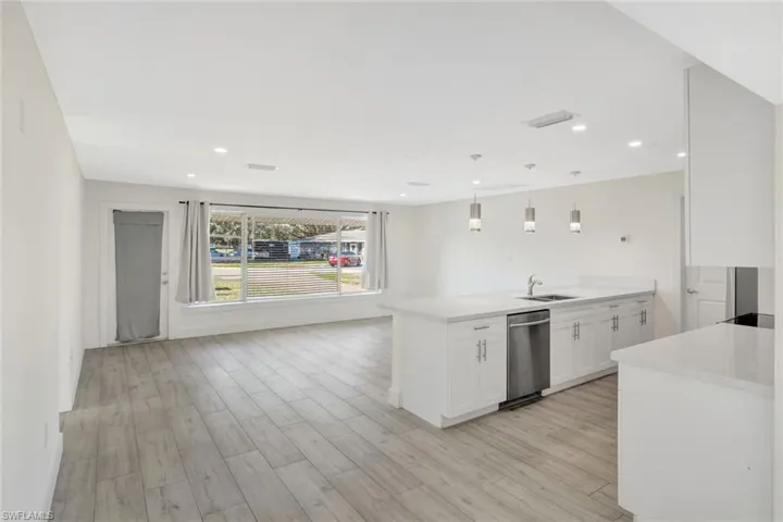 Kitchen featuring a peninsula, white cabinets, pendant lighting, light wood-style flooring, and light stone counters