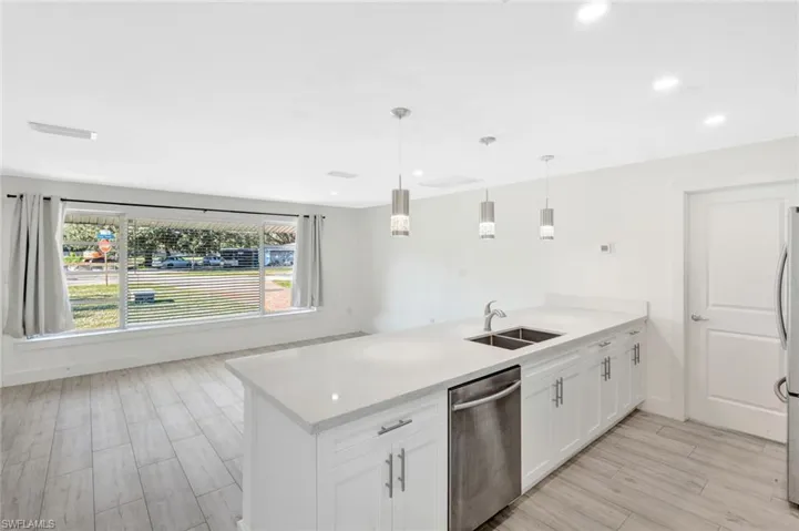 Kitchen with a peninsula, light wood-style flooring, appliances with stainless steel finishes, decorative light fixtures, and white cabinets