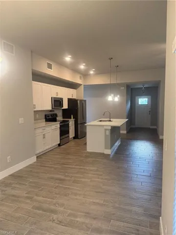 Kitchen featuring stainless steel refrigerator, sink, hanging light fixtures, a center island with sink, and range
