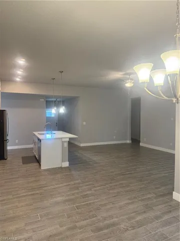 Kitchen with refrigerator, dark wood-type flooring, sink, a center island with sink, and hanging light fixtures