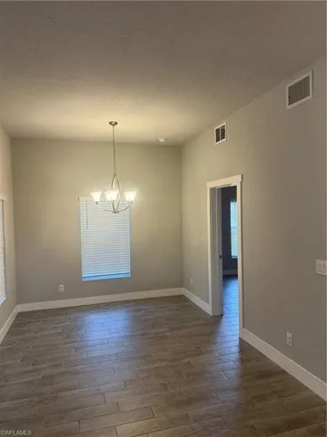Spare room featuring a textured ceiling, a notable chandelier, and dark wood-type flooring