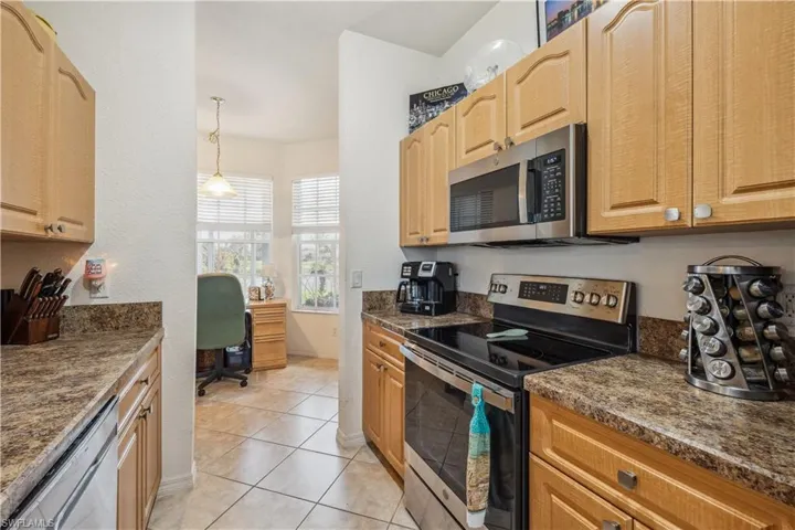 Kitchen featuring built in desk, light tile patterned floors, appliances with stainless steel finishes, light brown cabinets, and pendant lighting