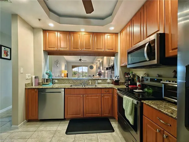 Kitchen featuring ceiling fan, appliances with stainless steel finishes, recessed lighting, a tray ceiling, and stone counters