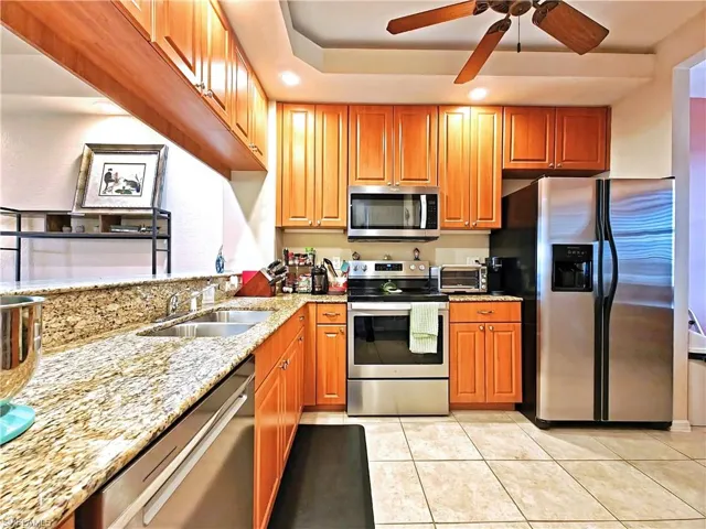 Kitchen with stainless steel appliances, light stone counters, light tile patterned floors, a ceiling fan, and recessed lighting