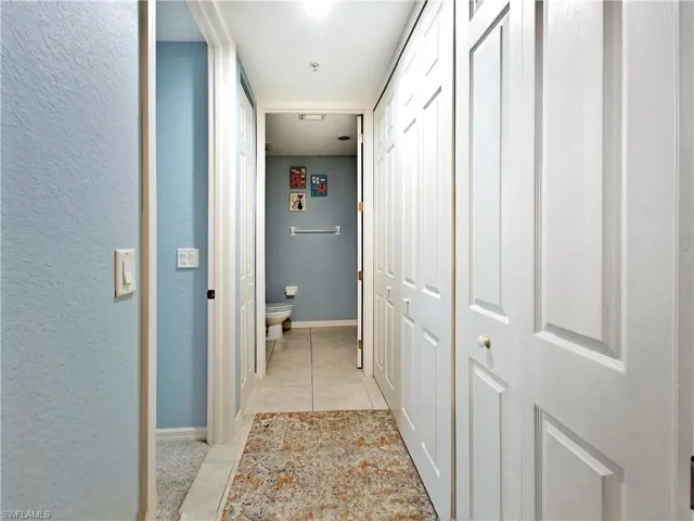 Corridor with light tile patterned flooring and a textured wall