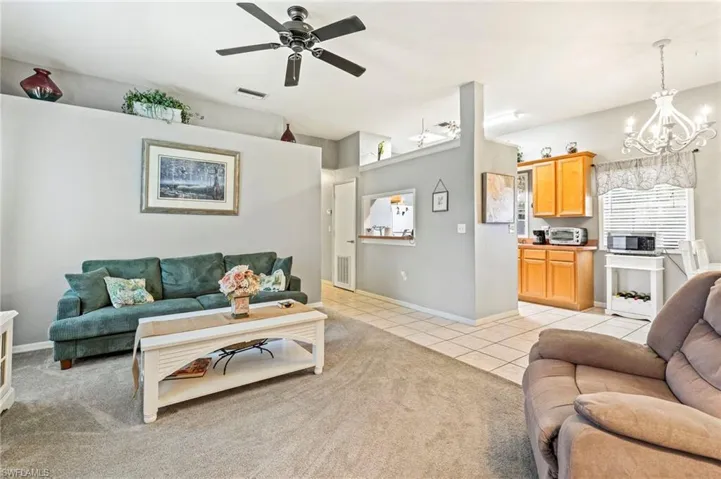 Living area with light tile patterned floors, a chandelier, ceiling fan, and light colored carpet