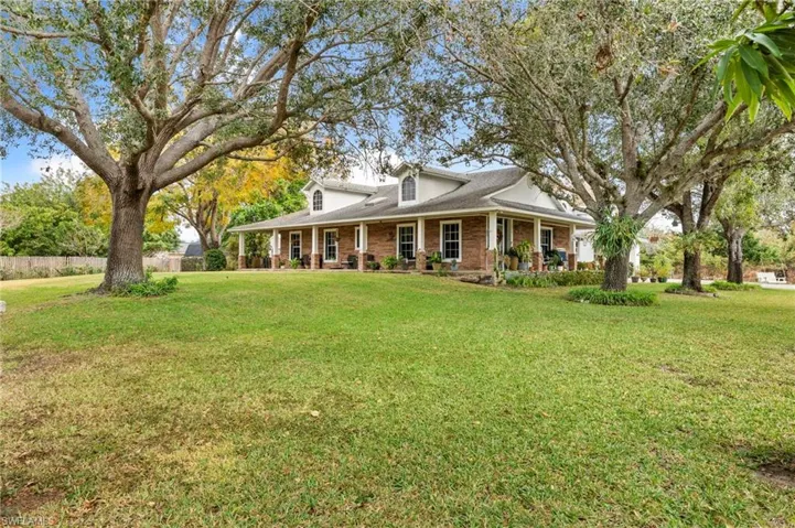 View of front facade with a large porch, brick siding, a front yard, and roof with shingles