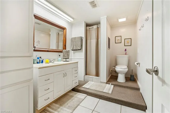 Bathroom with curtained shower, vanity, light tile patterned floors, and ornamental molding