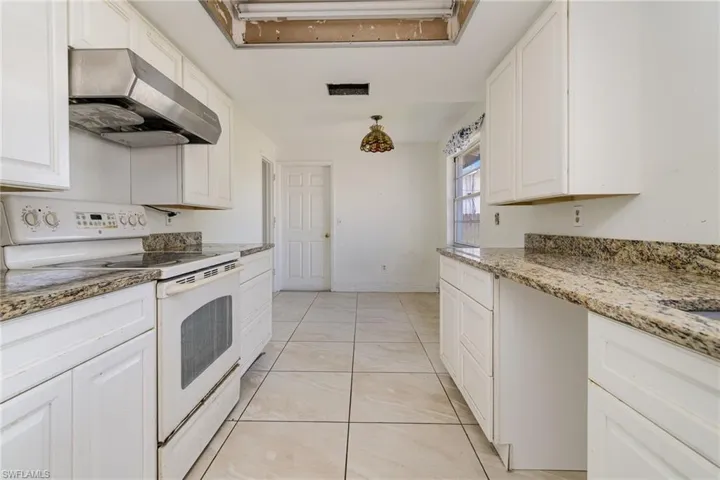 Kitchen featuring light stone counters, white range with electric stovetop, visible vents, white cabinetry, and under cabinet range hood