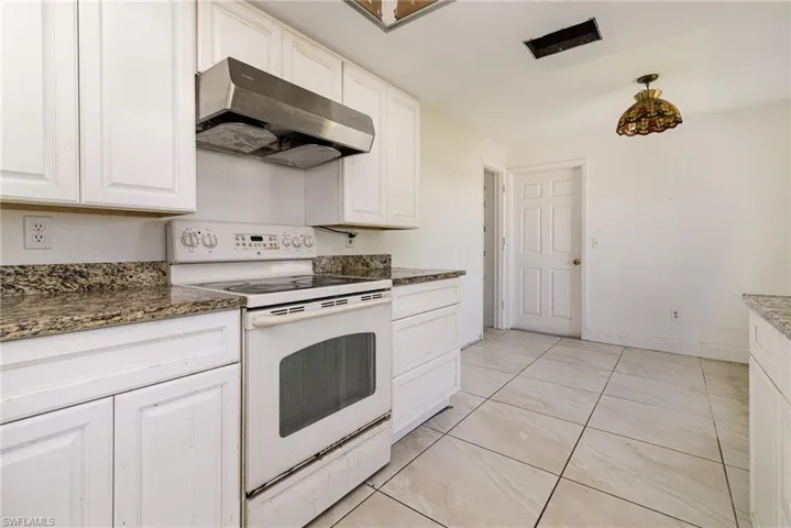 Kitchen with under cabinet range hood, white electric stove, white cabinetry, and dark stone countertops