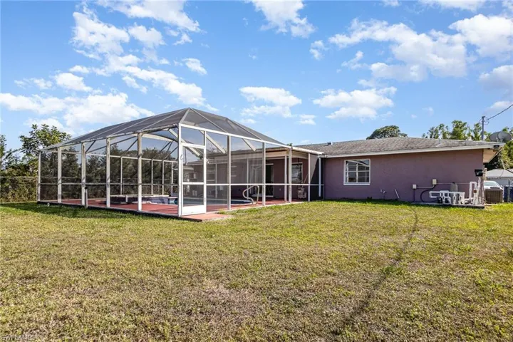 Rear view of house featuring a yard, stucco siding, a patio area, glass enclosure, and central AC