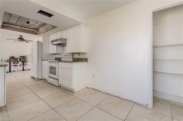 Kitchen featuring white appliances, dark countertops, ceiling fan, under cabinet range hood, and white cabinetry