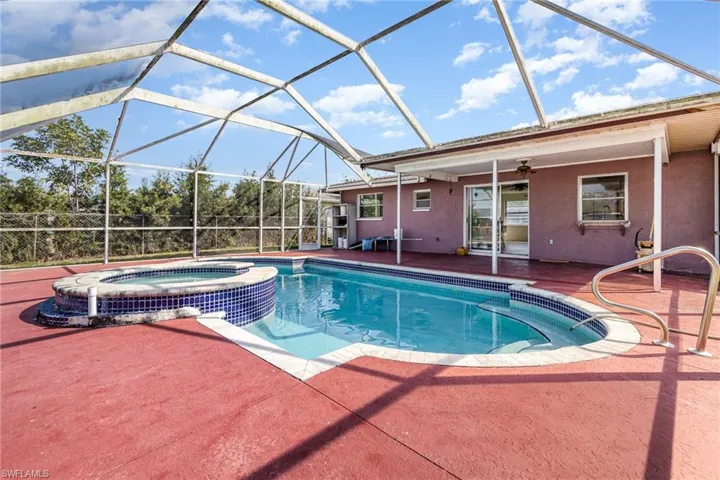 View of swimming pool featuring ceiling fan, glass enclosure, a patio, and a pool with connected hot tub