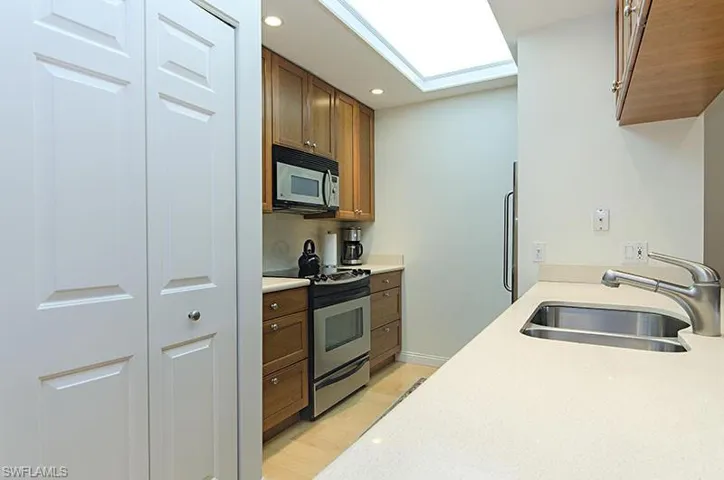 Kitchen with electric stove, white microwave, recessed lighting, brown cabinetry, and light stone countertops