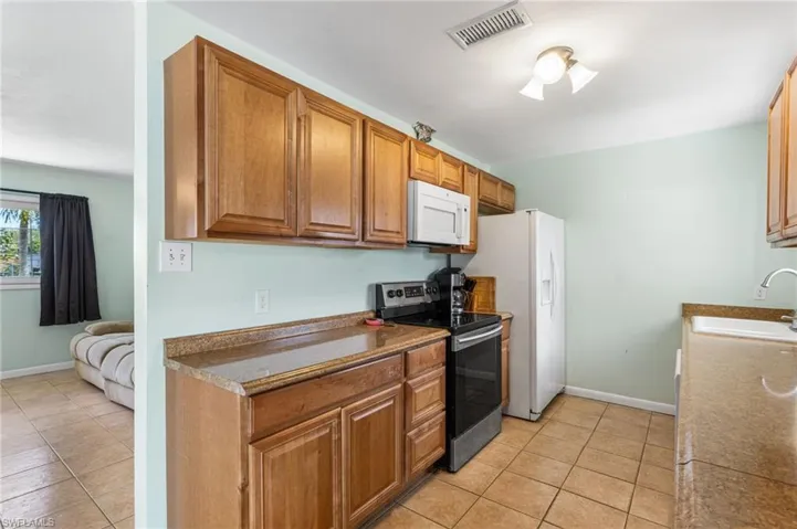 Kitchen with white appliances, wood finish cabinetry, light tile patterned floors, and dark countertops