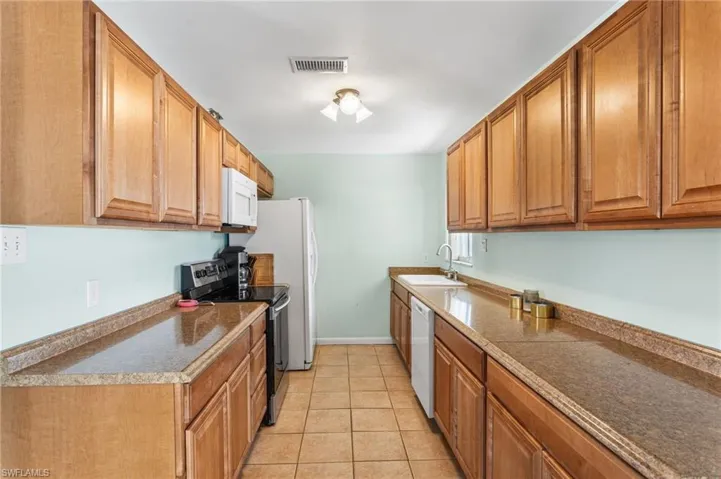 Kitchen featuring white appliances, wood finish cabinetry, light tile patterned flooring, and dark countertops
