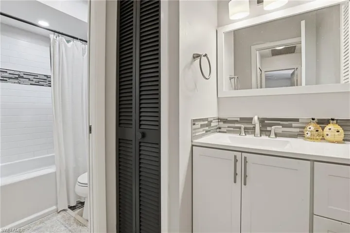 Bathroom with a closet, vanity, shower / bathtub combination with curtain, and tasteful backsplash