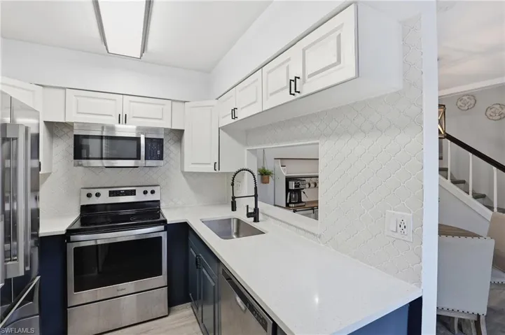Dual tone kitchen with dual tone cabinetry, stainless steel appliances, light stone countertops, decorative backsplash, and light wood-style flooring