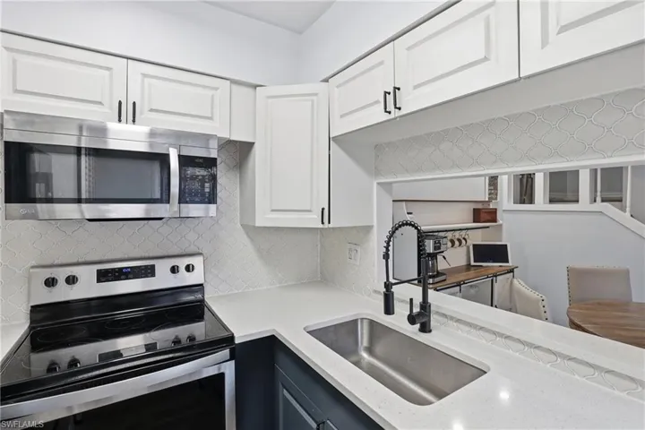 Kitchen with stainless steel appliances, white cabinetry, tasteful backsplash, and light stone counters