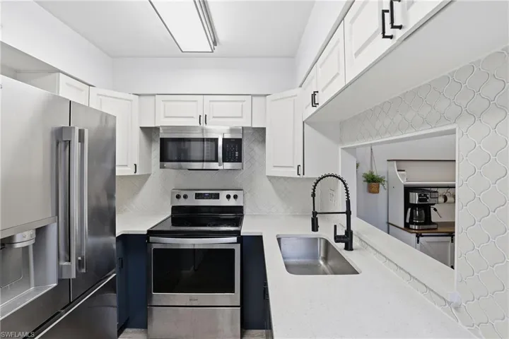 Kitchen featuring stainless steel appliances, white cabinetry, decorative backsplash, and light stone counters