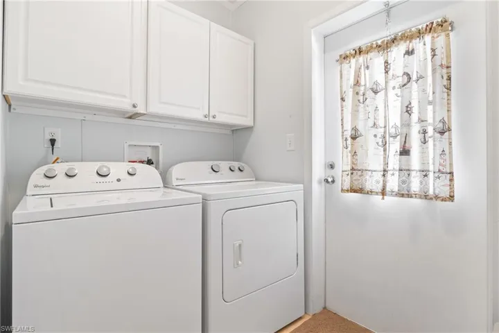 Clothes washing area with independent washer and dryer, light carpet, and cabinets
